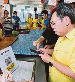  ?? [ FOTO MOHD LATIF AHMAD/BH] ?? Kui Hian menggunaka­n aplikasi Maybank QRPAY ketika berkunjung di Pasar Basah Batu 3, Kuching, kelmarin.