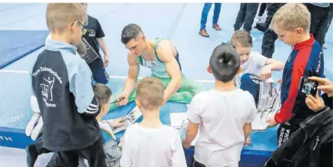  ?? FOTO: RUPPENTHAL ?? Nationaltu­rner Lukas Dauser (Mitte) gilt als Star zum Anfassen. Hier schreibt er Autogramme für Kinder am Rande eines Bundesliga-Wettkampfs der TG Saar. Ab der kommenden Saison wird Dauser aber nicht mehr für die Saarländer an die Geräte gehen.