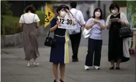  ?? Photograph: Eugene Hoshiko/AP ?? A tour guide waits to meet her group near a shopping street in Tokyo. Individual travellers will be able to visit Japan without visas from 11 October.