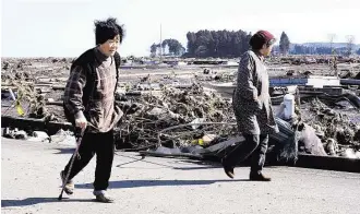  ?? Toru Yamanaka / AFP Getty Images ?? Residents wander past debris on March 12, 2011, the day after a massive quake and tsunami hit Japan. As reconstruc­tion gains ground, families fear missing victims’ remains might be buried forever.