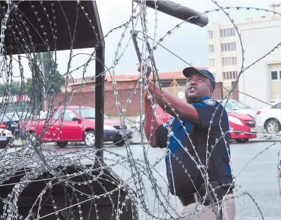  ?? Pictures: Alaister Russell ?? WEIGHTY TASK. A metro policeman removes barbed wire from outside the Boksburg Magistrate­s’ court yesterday, following the withdrawal of charges against Zanokuhle Mbatha, who was briefly accused in the murder of Bafana star Senzo Meyiwa.