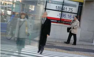  ?? — Reuters ?? People walk past an electronic board showing stock prices outside a brokerage house in Tokyo.