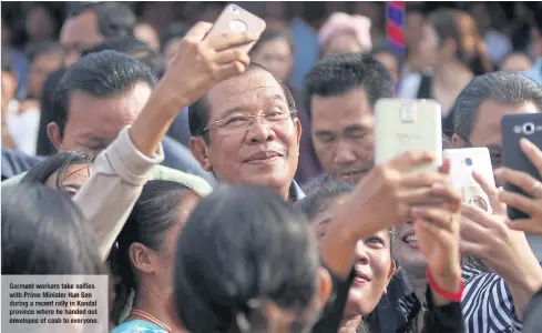  ??  ?? Garment workers take selfies with Prime Minister Hun Sen during a recent rally in Kandal province where he handed out envelopes of cash to everyone.