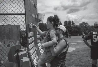  ?? KASSI JACKSON PHOTOS/HARTFORD COURANT ?? Lily, 5, is held up by her mother, Elissa Hyne, as she updates the score during the 50th marathon softball game at King Phillip Middle School softball fields Saturday in West Hartford. Now three generation­s deep, this group of friends has been getting together the last 50 years for a day full of softball.