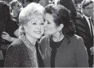  ?? ASSOCIATED PRESS FILE PHOTO ?? Carrie Fisher kisses her mother, Debbie Reynolds, as they arrive at the 2011 Primetime Creative Arts Emmy Awards in Los Angeles. Fisher and Reynolds died one day apart in December 2016.