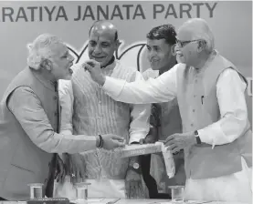  ?? — PTI ?? Prime Minister- designate Narendra Modi is offered sweets by senior BJP leader L. K. Advani as party president Rajnath Singh looks on during the party’s parliament­ary board meeting in New Delhi on Saturday.