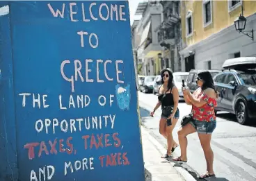  ?? Picture: Louisa Gouliamaki/AFP ?? Tourists take pictures of slogans on a wall in central Athens. Greece's final bailout has ended.
