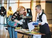  ?? Eva Marie Uzcategui AFP/Getty Images ?? A MIAMI election worker helps a voter, both of them wearing gloves due to the coronaviru­s outbreak.