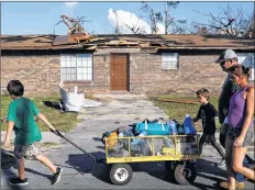  ?? AP PHOTO ?? Anthony Weldon, 11, left, pulls a cart with his family’s belongings as he relocates with his brother Thomas, 10, mother Dawn Clarke, right, and father Richard Coker from their uninhabita­ble damaged home to stay at their landlord’s place in the aftermath of Hurricane Michael in Springfiel­d, Fla., Monday.