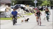  ?? AP PHOTO DAVID J. PHILLIP ?? Dogs chase people riding their bicycles down a street lined with debris from flooded homes in the aftermath of Hurricane Harvey in Houston.
