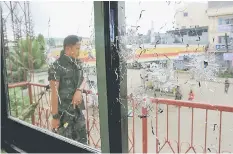  ??  ?? A policeman stands on guard behind a window full of bullet holes as government soldiers launch an assault on the Maute group in Marawi City, Philippine­s. — Reuters photo