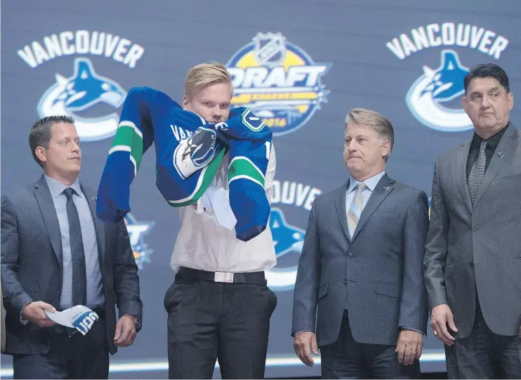  ?? — THE CANADIAN PRESS FILES ?? Olli Juolevi, fifth overall pick, puts on his sweater as he stands on stage with members of the Vancouver Canucks management team at the NHL draft in Buffalo, N.Y. in June. While any other year Juolevi would have been seen as a major win, his...