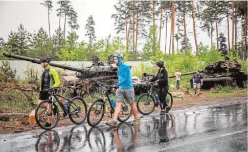  ?? // AFP ?? Tres ciclistas pasan por delante de los restos de dos tanques rusos a las afueras de Kiev