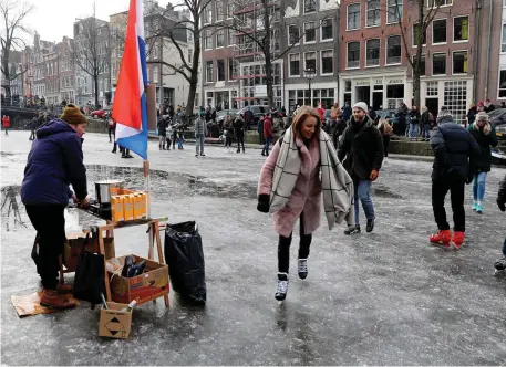  ??  ?? A hot-chocolate seller watches as ice skaters skate and walk on the frozen Prinsengra­cht canal during icy weather in Amsterdam. Photo: Reuters