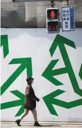  ?? —AFP ?? TOKYO: A pedestrian walks past decorated panelling used to shroud a constructi­on site along a street in Tokyo yesterday.