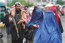  ?? AP ?? Women in all-covering burqa pass by a Taliban fighter in Kabul’s old market.