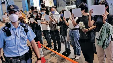  ?? | Reuters ?? PEOPLE hold white sheets of paper and flowers as police check their IDs during a protest over Covid-19 restrictio­ns in mainland China, during a commemorat­ion of the victims of a fire in Urumqi, in Hong Kong, yesterday.