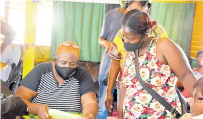  ??  ?? President of the Harbour Street Craft Market, Melody Haughton (seated), tends to some of the members of her associatio­n who have grown weary of awaiting state benefits tied to the coronaviru­s pandemic.