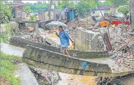  ?? PTI PHOTOS ?? A man walks on a damaged bridge as collapsed houses are also seen following a flash flood at Kalika Colony in Jammu on Thursday; and (below) a car buried in debris after a landslide .