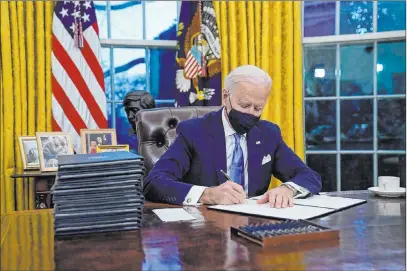  ?? Evan Vucci The Associated Press ?? Shortly after his swearing-in, President Joe Biden signs a stack of executive orders Wednesday in the Oval Office.