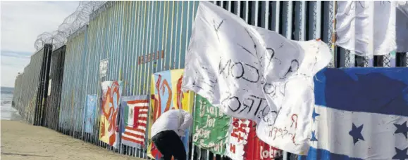 ??  ?? Joseph, a migrant from Honduras, plants a white flag with the words, “Peace and God with us”, in front of the border wall during an art display on the border wall, topped with razor wire, Tuesday, January 8, 2019, on the beach in Tijuana, Mexico. Ready to make his case on prime-time TV, President Donald Trump is stressing humanitari­an as well as security concerns at the Us-mexico border as he tries to convince America he must get funding for his long-promised border wall before ending a partial government shutdown that has hundreds of thousands of federal workers facing missed pay cheques.