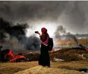  ?? SPENCER PLATT / GETTY IMAGES ?? A Palestinia­n woman documents the clash along the border fence with Israel as demonstrat­ions continue Monday in Gaza City. Israeli soldiers killed at least 52 Palestinia­ns and wounded more than 2,400.
