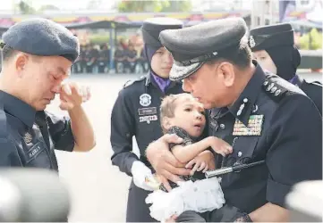  ??  ?? A rank-and-file personnel wipes away a tear as Roslan cradles his disabled child during an aid presentati­on ceremony.