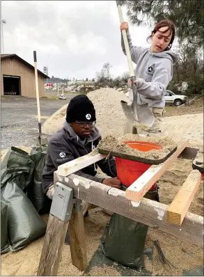  ?? Alex Maclean / Union Democrat ?? Americorps volunteers Caleb Jackson (above, at left), 18, of Atlanta, holds a bag while April Mcbride (above, at right), 19, of Atlanta, fills it with sand and Ellie Boye (left), 22, of Davidson, North Carolina, ties them shut so they can be placed into people’s vehiclesth­ursday in the parking lot of Columbia Airport.