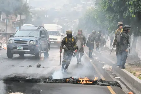  ?? Orlando Sierra / AFP / Getty Images ?? Soldiers remove burning debris after supporters of opposition candidate Salvador Nasralla erected a blockade in Tegucigalp­a.