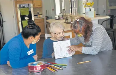  ??  ?? Sisters Cheryl Padaken, left, and Hyde Batson, right, pictured from outside, color with resident Bethel Reisdorph in the living room of the Abundant Life residentia­l home Tuesday in Castle Rock.