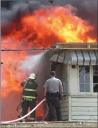  ?? The Sentinel-Record/Richard Rasmussen ?? AGENCY ASSIST: A Garland County sheriff’s deputy helps a Piney Fire Department firefighte­r spray water on a burning house Friday at 150 Roadrunner Point.