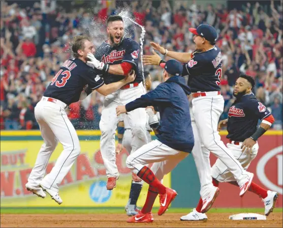  ?? The Associated Press ?? Cleveland Indians’Yan Gomes, second from left, is hugged by pitcher Josh Tomlin and mobbed by teammates after Gomes hit a game winning RBI-single in the 13th inning of Game 2 of their American League Division Series against the New York Yankees on...
