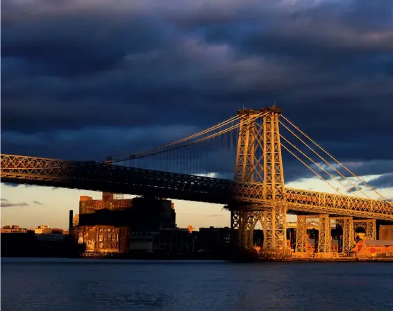  ??  ?? Licht und Schatten
New York, East River, Williamsbu­rg Bridge: Ein Wolkenkrat­zer wirft einen fast bedrohlich wirkenden Schatten auf die Brücke und die Häuser in Brooklyn. Der rechte Brückenabs­chnitt wirkt wie von einem Bühnenspot beleuchtet.