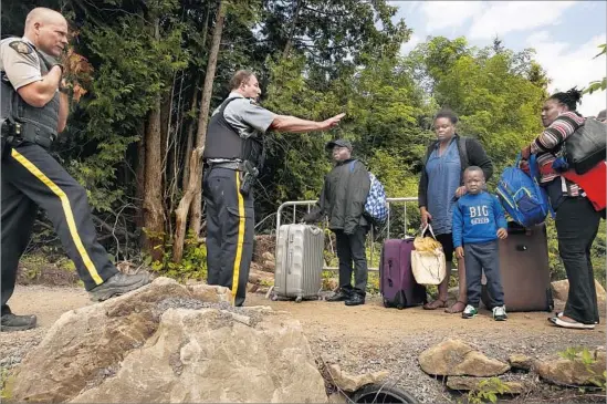  ?? PHOTOGRAPH­S by CAROLYN COLE Los Angeles Times ?? SGT. MICHAEL HARVEY, center, of the Royal Canadian Mounted Police, stops a group of Haitians before they cross the border in Champlain, N.Y.