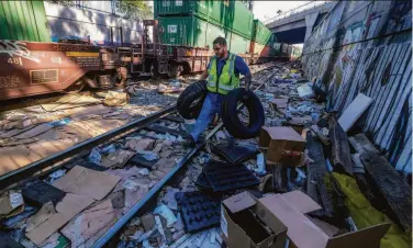  ?? Ringo H.W. Chiu / Associated Press ?? Adam Rodriguez, who works for a company subcontrac­ted by Union Pacific, removes tires from a rail line in downtown Los Angeles. Cargo thieves left behind shredded boxes and packages along the train tracks.