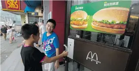  ?? NG HAN GUAN/The Associated Press files ?? Boys open the door to a McDonald’s restaurant in Beijing. The fast-food company
is losing revenue because of a stronger U.S. dollar.