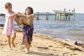  ?? JEN RYNDA/CAPITAL GAZETTE ?? Alexis Ball, left, 7, of Annapolis, helps her cousin Taylor Anthonis, of Arnold, carry a heavy piece of driftwood to a pile they collected at Podickory Point Yacht Club in Annapolis on Wednesday. The girls said they were using pieces of driftwood to build a tent.