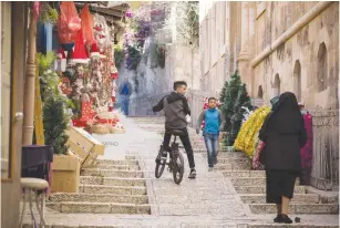  ?? (Hadas Parush/Flash90) ?? PEOPLE PASS BY a store selling Christmas decoration­s in the Christian Quarter of Jerusalem’s Old City, in 2019.