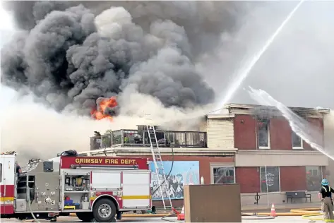  ?? GRANT LAFLECHE/STANDARD STAFF ?? Heavy smoke and flames burst from the roof of a building on Main Street in Grimsby Thursday.
