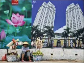  ?? DITA ALANGKARA — THE ASSOCIATED PRESS FILE ?? In this file photo, a snack and fruit vendor waits for customers near the advertisem­ent board of a shopping mall and apartment building in Ho Chi Minh City, Vietnam. Vietnam, the location of U.S. President Donald Trump’s next meeting with North Korean leader Kim Jong Un, has come a long way since the U.S. abandoned its war against communist North Vietnam in the 1970s.