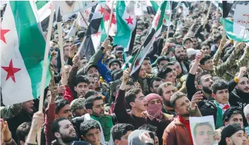  ?? (Khalil Ashawi/Reuters) ?? YOUNG SYRIAN men in opposition-held Idlib carry banners and flags during a rally last month to mark the 10th anniversar­y of the start of the civil war in Syria.