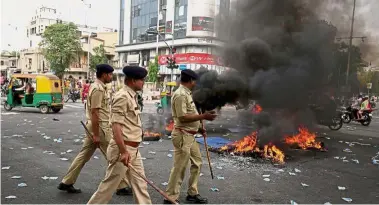  ??  ?? Keeping the
peace: Police officers patrolling a street after people belonging to the Dalit community burned tyres and hoardings during the strike in Ahmedabad. — Reuters