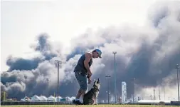  ?? MARIE D. DE JESÚS THE ASSOCIATED PRESS ?? Ray Moore trains his dog, Aries, with a cloud of smoke in the background from the chemical fire in Port Neches, Texas. Three workers were hurt in the first blast.