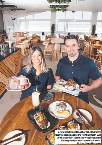  ?? ?? A new beachfront tapas bar called Sandfire recently opened above the North Burleigh Surf Life Saving club. Staff Skye Woodbridge and Christophe­r Que with some of the menu. Picture: Glenn Hampson