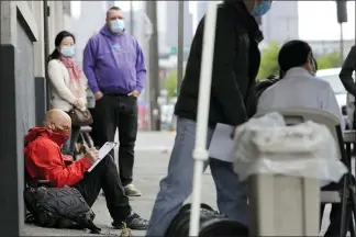  ?? THE ASSOCIATED PRESS ?? Glen Buhlmann, lower left, fills out a job applicatio­n during a walk- and drive-up job fair in Seattle for clothing maker Outdoor Research’s new line of face masks and other personal protection equipment the company has started manufactur­ing due to the coronaviru­s pandemic. U.S. employers likely rehired several million more workers in June, thereby reducing a Depression-level unemployme­nt rate.