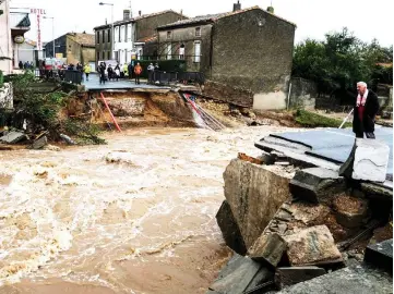  ??  ?? People stand on the road by a bridge over the Trapel river that collapsed Villegailh­enc in the Aude department.