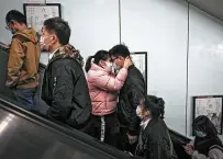  ??  ?? A couple wearing face masks to help curb the spread of the coronaviru­s hug each other as they exit a subway station with other commuters.