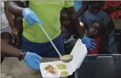 ?? ODELYN JOSEPH — THE ASSOCIATED PRESS ?? A server ladles soup into a container as children line up to receive food at a shelter for families displaced by gang violence in Port-au-Prince, Haiti, Thursday.