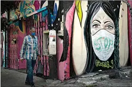  ?? JAE C. HONG / AP ?? A man wearing a face mask walks past a mural in South Central Los Angeles on Thursday. President Donald Trump’s startling COVID-19 diagnosis serves as a cruel reminder of the pervasive spread of the coronaviru­s in the United States and shows how tenuous of a grip the nation has on the crisis, health experts said.