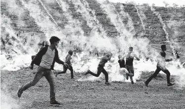  ?? Abbas Momani / AFP / Getty Images ?? Palestinia­n demonstrat­ors run from tear gas fired by Israeli troops during a protest against Jewish settlement­s Friday in the village of al-Mughayyir in the Israeli-occupied West Bank.